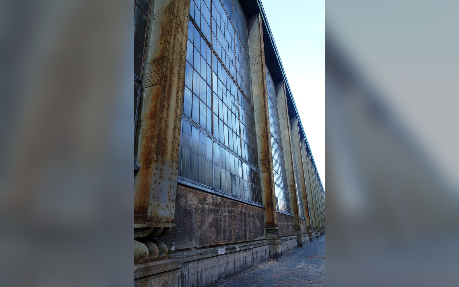 Rusted steel columns support rows of tall industrial windows along a factory facade