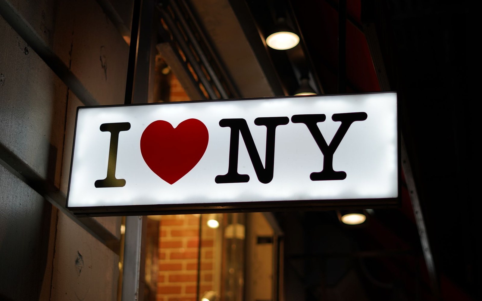 An illuminated "I heart NY" sign hangs above a storefront entrance at night