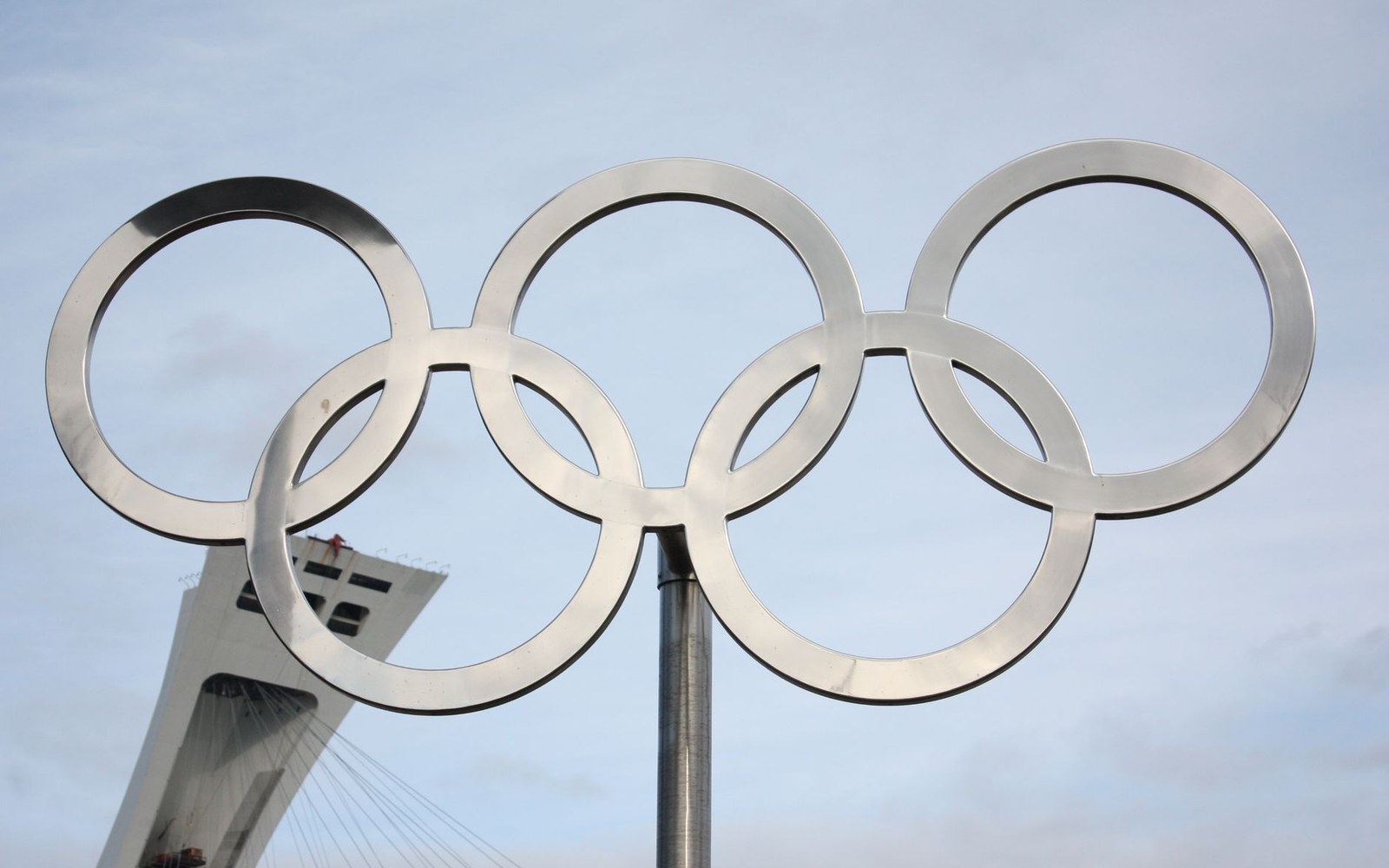 Metal Olympic rings sculpture stands against the sky with the Montreal Tower visible behind