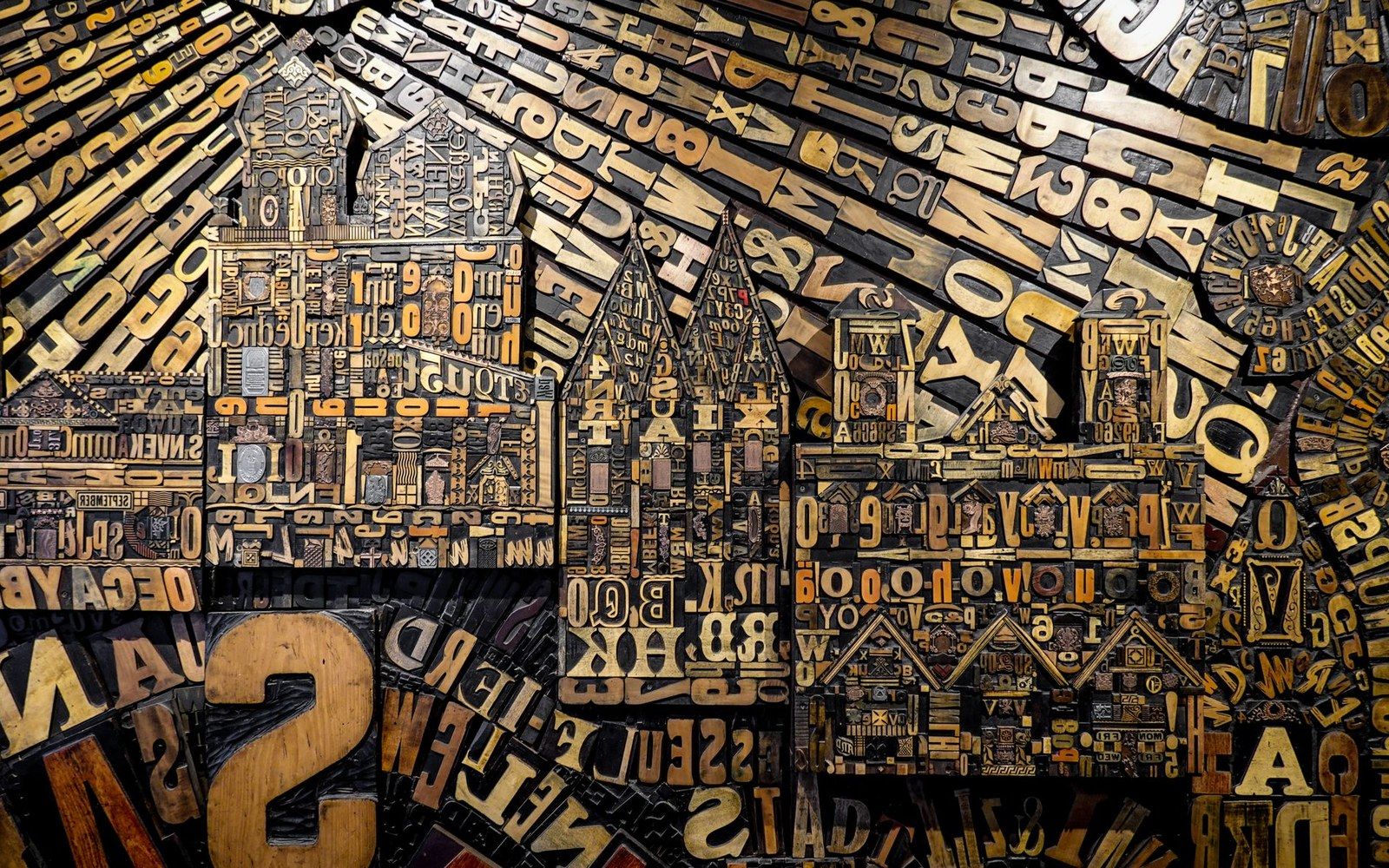 A letterpress forme with metal type locked into a chase, shot close under raking side-light that picks out the face height and the furniture between lines