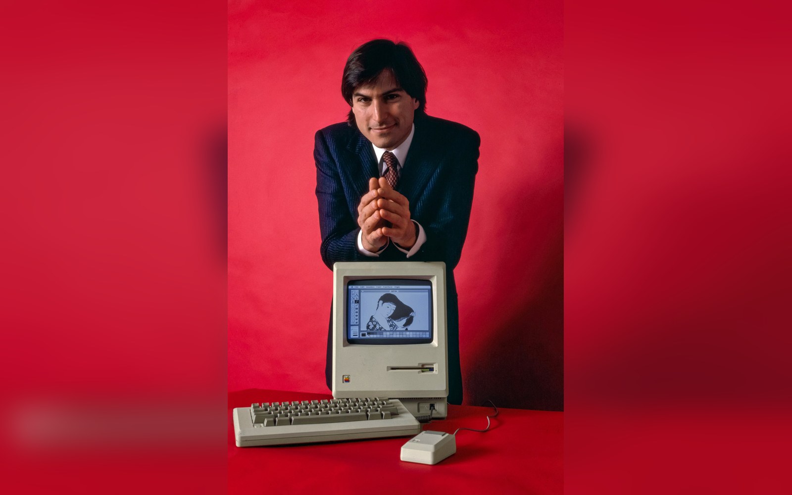 A 128k Macintosh screen displaying the original 1984 desktop with the trash can, disk icon, and menu bar, photographed straight-on