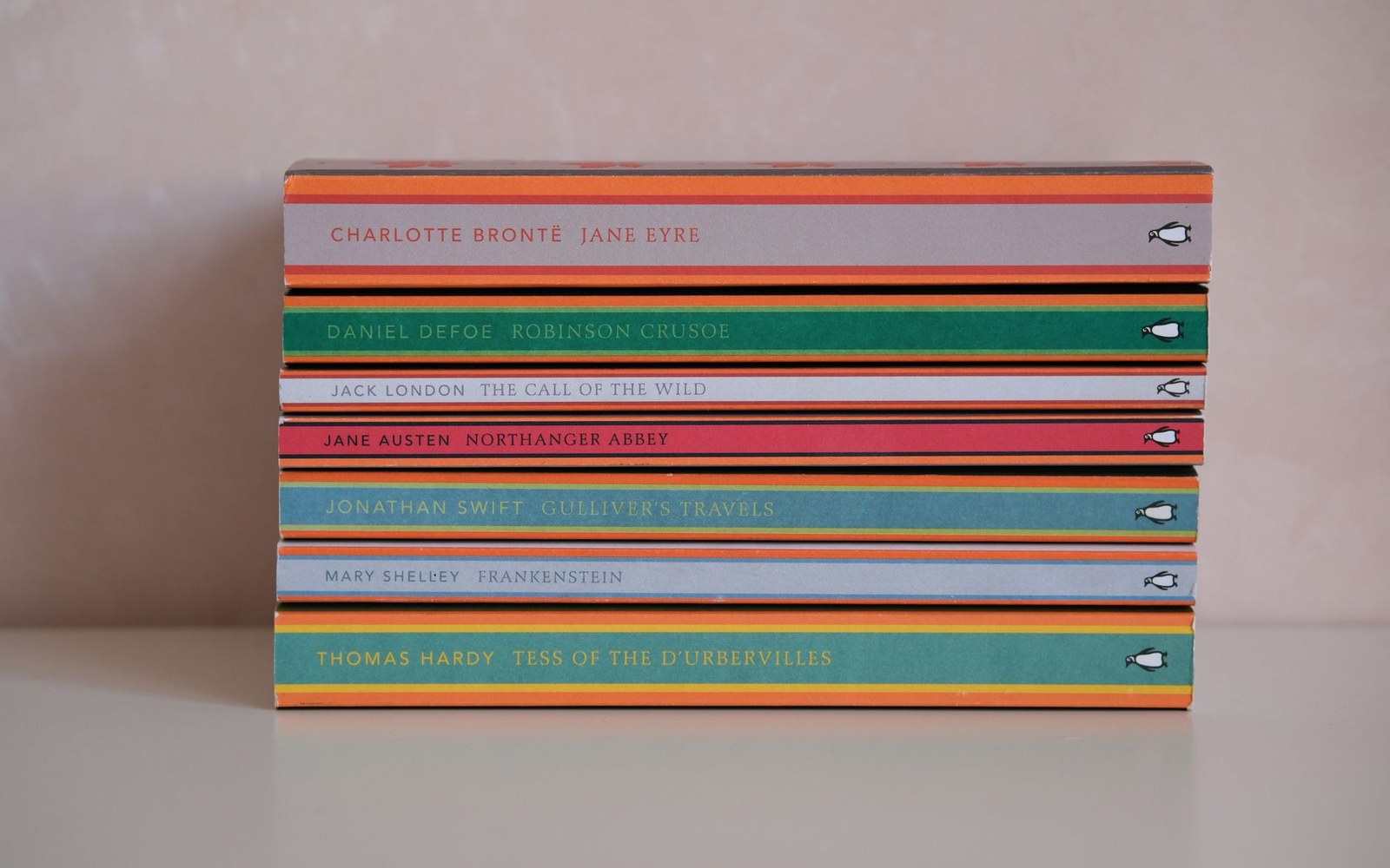 Three Penguin paperbacks in the Tschichold-era tripartite covers — orange, green, blue — laid face-up on a white surface